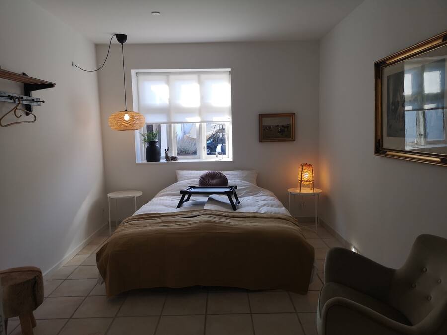 A bedroom with a bed, bedside lamps, a window, and a chair.