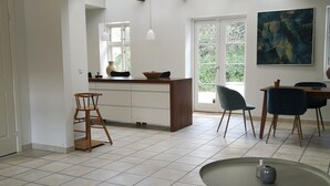 A spacious living area with a kitchen, a dining table with chairs, and a large window providing natural light. - MidtGolf Guest house (Regstrup)