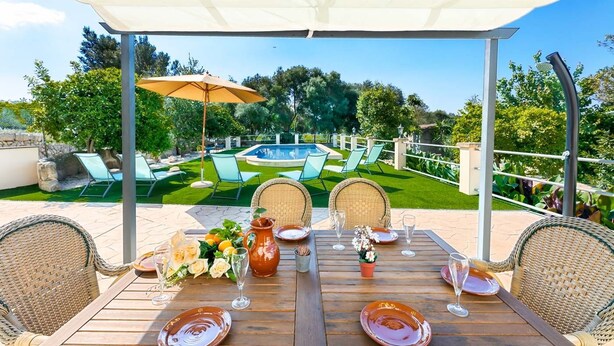 A patio with a table set for dining, surrounded by wicker chairs, a pool, and a well-maintained lawn. - CA SA Lloritana - 6 pax, private pool, wifi free! (Sencelles)