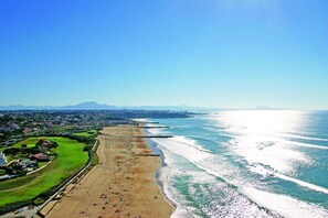 Vista aérea de una zona costera con playa, campo de golf y edificios residenciales al fondo.
