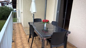 A patio with a table and chairs, a white umbrella, and a vase with red flowers.