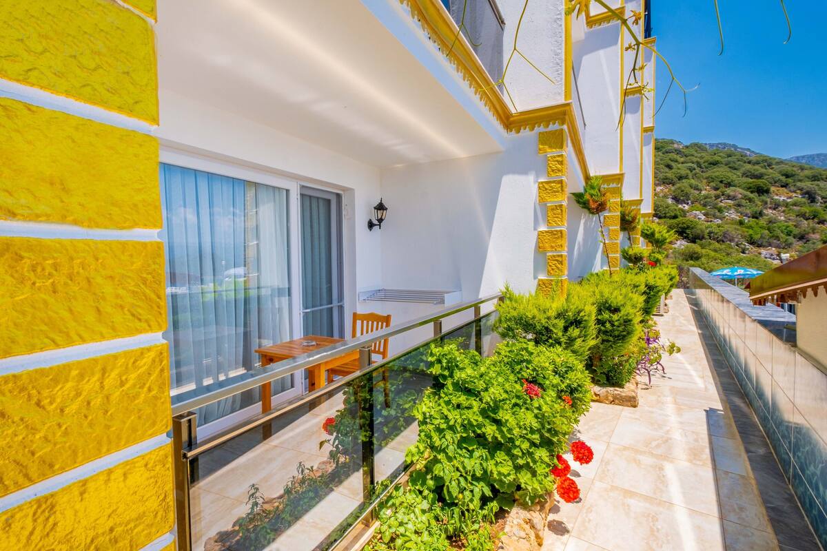 A balcony with a glass railing, a wooden table, and chairs. There is a window with curtains and a door.