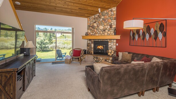 A cozy living room with a stone fireplace, a large window, and a wooden ceiling.