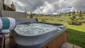 A hot tub on a wooden deck with a grassy yard and trees in the background.