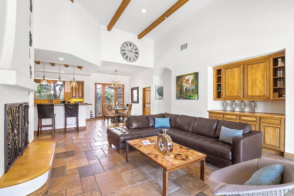 A spacious living area with a leather sofa, a coffee table, and a dining area with chairs and a chandelier.