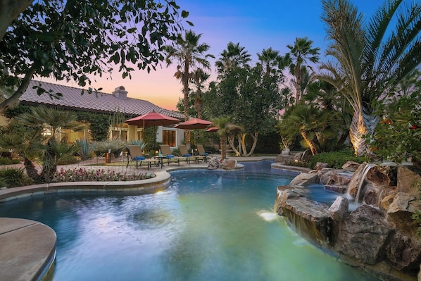 A resort pool area with lounge chairs, umbrellas, and a waterfall feature.