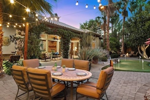 An outdoor patio with a round table and chairs, surrounded by lush greenery and palm trees.