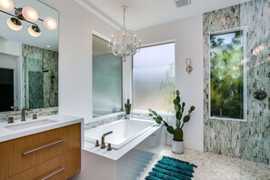 A modern bathroom with a large mirror, a white bathtub, a vanity with a sink, and a chandelier. - The Bird House - Swanky Poolside Paradise (Rancho Mirage)