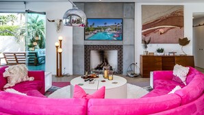 Een moderne woonkamer met een open haard, een tv met uitzicht op het zwembad en een levendig roze bank.