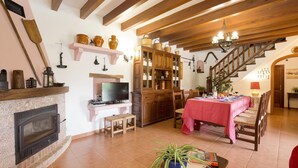 A living room with a fireplace, wooden beams, a dining table with a red tablecloth, and a staircase. - ASSUMPCIO. Pretty villa close to Pollensa (Pollensa)