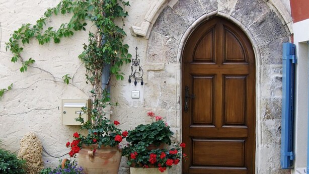 Edificio de piedra con puerta de madera, plantas en macetas y un aplique de pared.