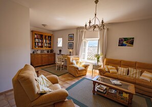 A living room with a sofa, armchair, coffee table, bookshelf, and a dining area with a table and chairs. - La Maison des Pèlerins (Sablet)