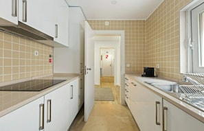A narrow kitchen with white cabinets, a black countertop, and a window.