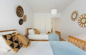 Ett sovrum med två sängar, en hängande lampa och dekorativ väggkonst.