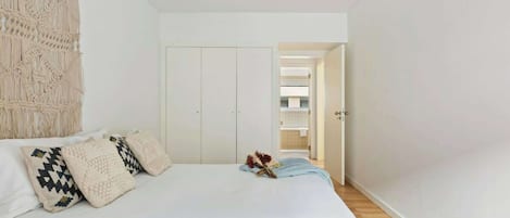 A bedroom with a bed, pillows, a macrame wall hanging, and a door leading to a bathroom.