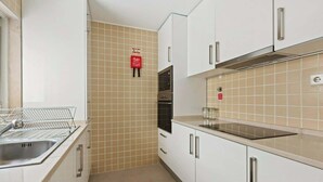 Une cuisine avec des meubles blancs, un évier en acier inoxydable, un four double et un dosseret carrelé.