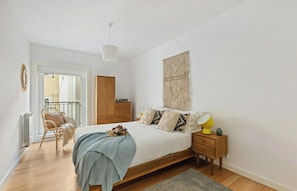 Quarto com cama, mesa de cabeceira, abajur e vista para o exterior.