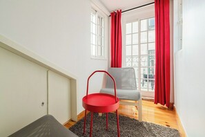 A room with a red chair, a grey chair, and a window with red curtains.