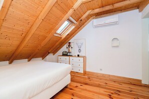 A bedroom with a sloped ceiling, a bed, a dresser, and a wall-mounted air conditioning unit. - Bairro Alto Attic Apartment With Balcony (Lisboa)