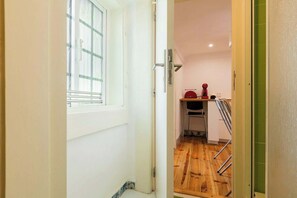A narrow hallway leading to a kitchen with a wooden floor, a radiator, and a red appliance on the counter. - Bairro Alto Attic Apartment With Balcony (Lisboa)