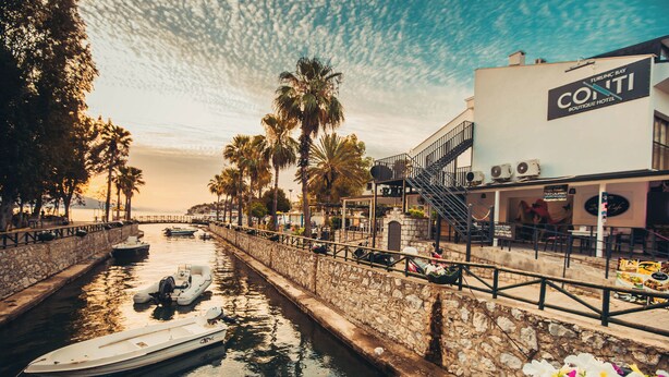 A waterfront hotel with a stone wall, a boat docked on the water, and a sign for the hotel. - Turunc Bay Conti Boutique Hotel (Marmaris)
