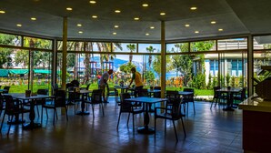 An indoor dining area with tables and chairs, large windows, and a view of greenery and buildings outside. - Turunc Bay Conti Boutique Hotel (Marmaris)
