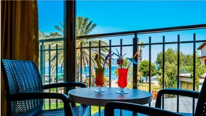 A balcony with two chairs and a table, a drink on the table, and a view of palm trees and a building. - Turunc Bay Conti Boutique Hotel (Marmaris)