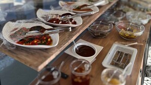 A food service area with various dishes and condiments on wooden tables, viewed through a glass window. - My Dream Bozcaada (Bozcaada)