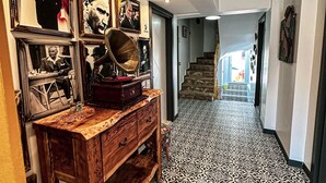A hallway with patterned flooring, a wooden console table with vintage items, framed pictures on the walls, and a staircase in the background. - My Dream Bozcaada (Bozcaada)
