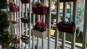 A covered outdoor area with vertical wooden railings holding various flower baskets. - My Dream Bozcaada (Bozcaada)