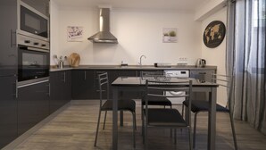 A modern kitchen with dark cabinetry, a stainless steel range hood, a dining table with four chairs, and a world map on the wall. - ANGEL'S SUNSET T2 ESTRITO DA CALHETA (Estreito da Calheta)