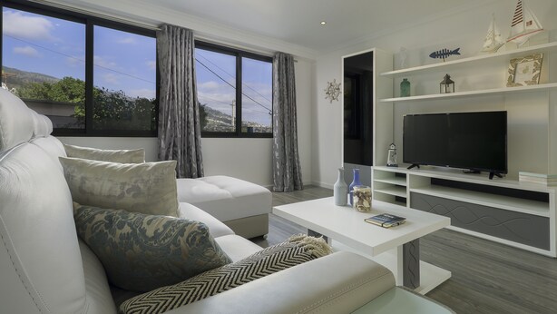 A modern living room with a white sofa, a flat-screen TV, and a bookshelf. - ANGEL'S SUNSET T2 ESTRITO DA CALHETA (Estreito da Calheta)
