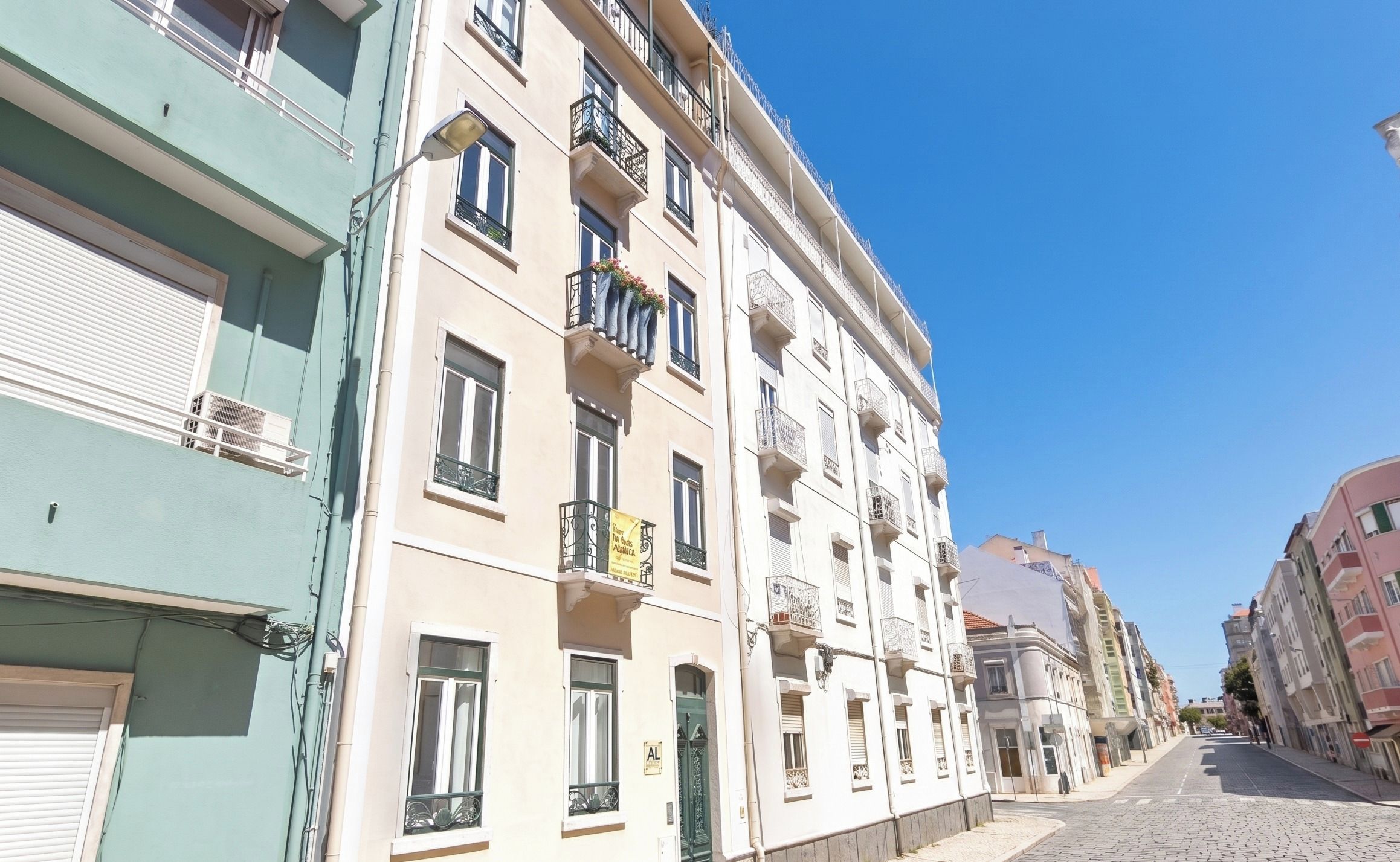 Un immeuble à plusieurs étages doté de balcons, un ciel dégagé et une rue pavée.
