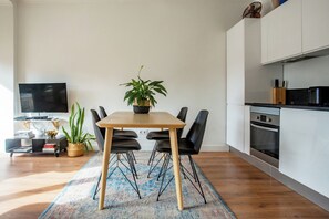Ein modernes Wohnzimmer mit Esstisch, Stühlen, einem Flachbildfernseher, einer Küchenzeile und einer Topfpflanze.