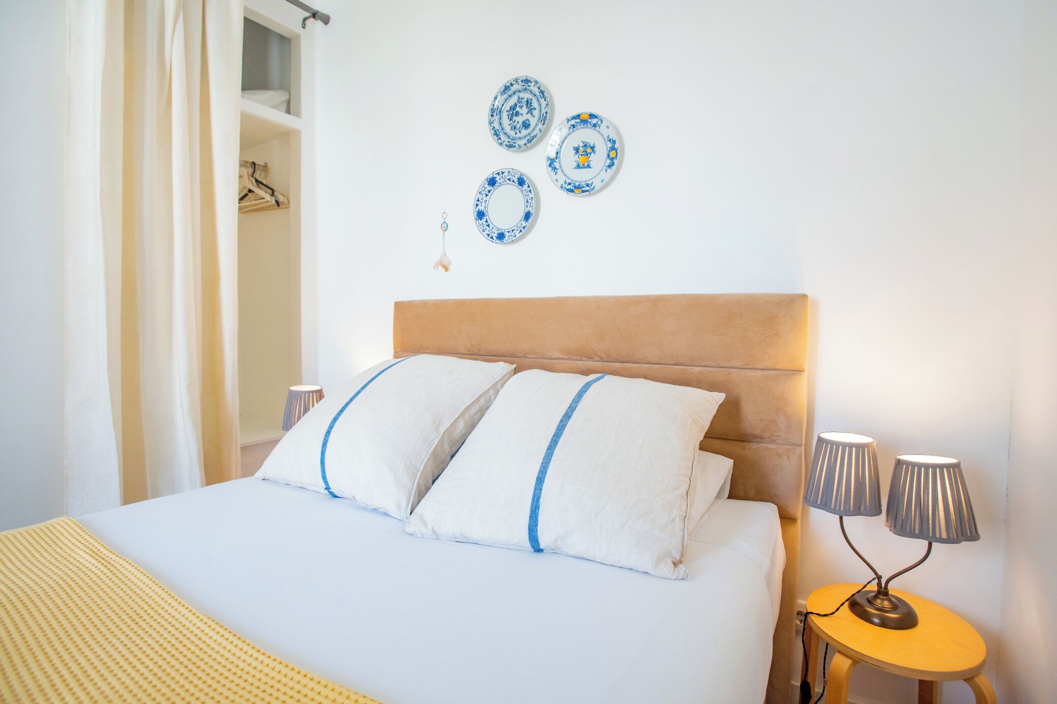 A hotel room with a bed, pillows, a nightstand, a lamp, and decorative plates on the wall.