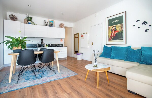 Un salon moderne avec un canapé blanc, un coin repas comprenant une table et des chaises, et une cuisine en arrière-plan.