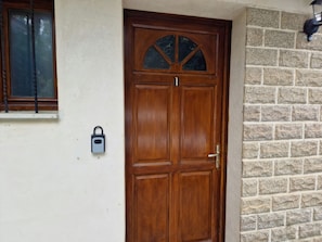 A wooden front door with a glass panel, a keypad lock, and a window with blinds.
