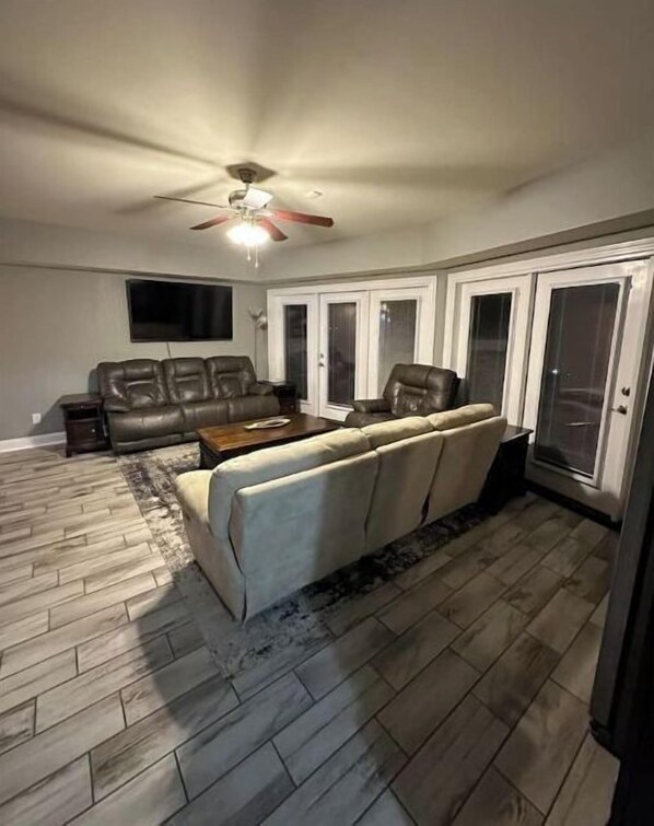 Relax in this spacious living room with a high ceiling, featuring a large sectional sofa and a smaller couch, both positioned against a wall with a large window.