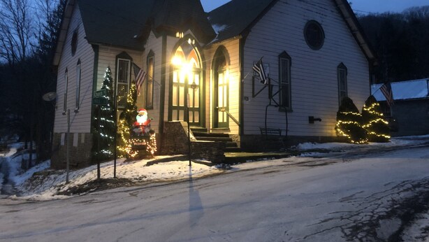 Una iglesia con campanario, porche delantero y luces navideñas.