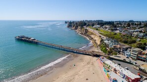 A coastal town with a pier extending into the ocean, beachfront properties, and a clear sky. - Pink Venetian (lower unit) (Capitola)