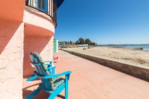 A balcony with two blue chairs, a pink wall, and a beach view.