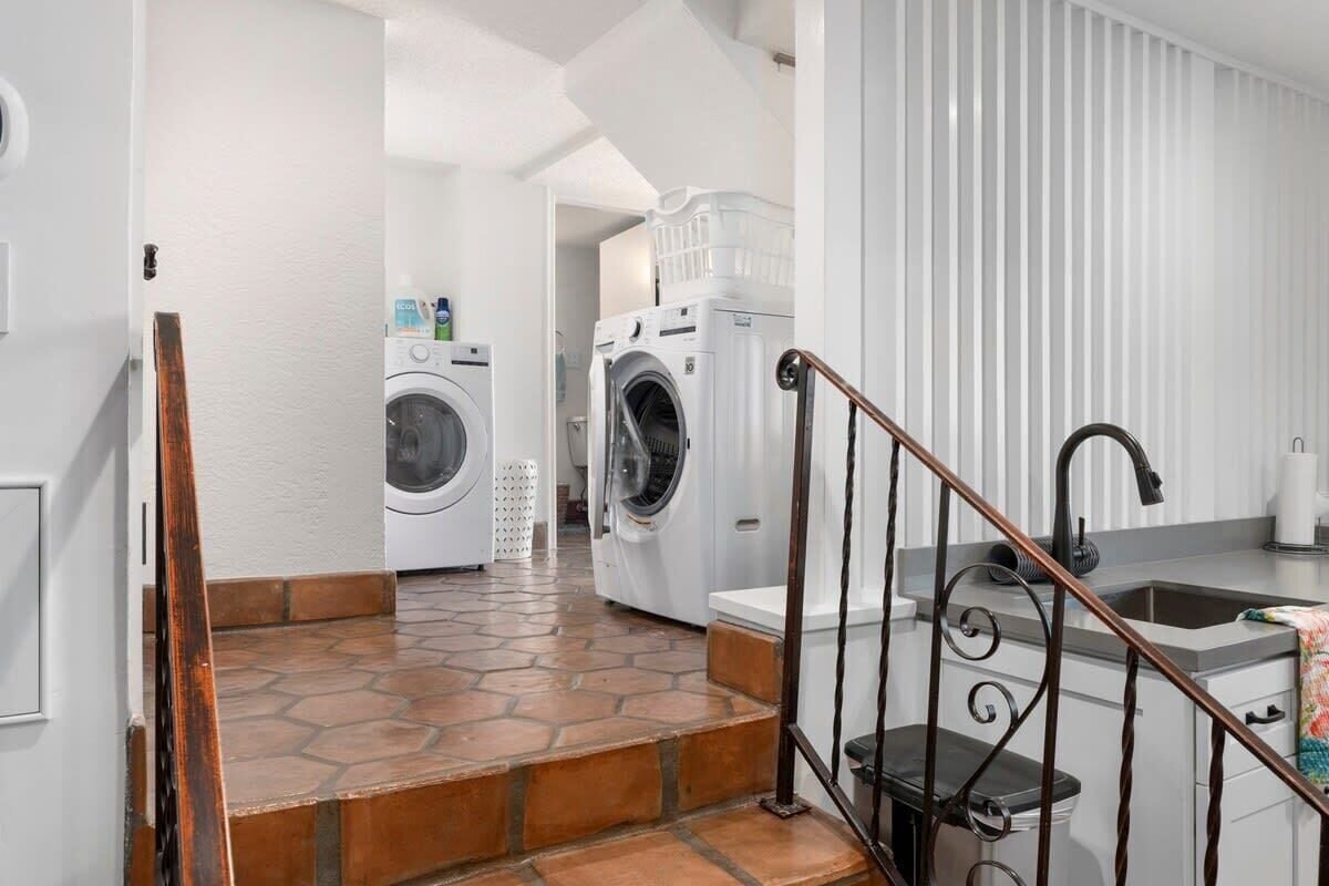 A laundry area with two washing machines, a sink, and a staircase with a metal railing.