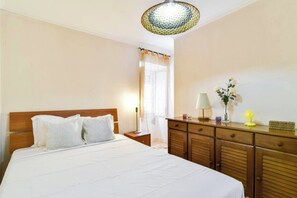 Een hotelkamer met een bed, een houten dressoir, een lamp en een vaas met bloemen.