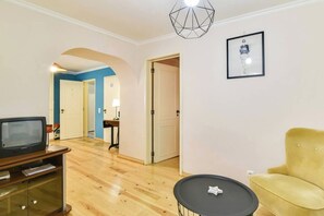 Ein Wohnzimmer mit Fernseher, einem gelben Sessel, einem kleinen Tisch und einem gerahmten Bild an der Wand.