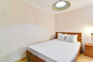 Ein Schlafzimmer mit einem hölzernen Bett, weißer Bettwäsche, einer Nachttischlampe und einer Deckenleuchte mit Struktur.