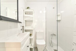 Een moderne badkamer met een douchecabine van glas, een wit toilet en een wastafel met spiegel.