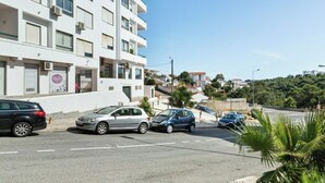 Un immeuble à plusieurs étages avec une façade blanche, des voitures garées dans la rue et un ciel bleu dégagé.