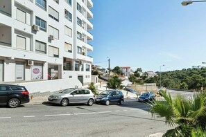 A multi-story building with a white facade, parked cars on the street, and a clear blue sky. - 2BD Duplex Apt Terrace- Cascais (Alcabideche)