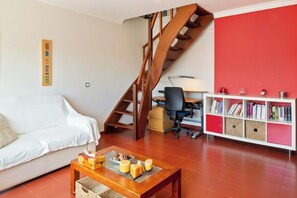 Una sala de estar con escalera de madera, un sofá blanco, una mesa de centro de madera con velas y una estantería llena de libros.
