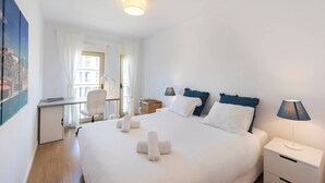 A hotel room with a large bed, a desk, a chair, and a nightstand with a lamp.